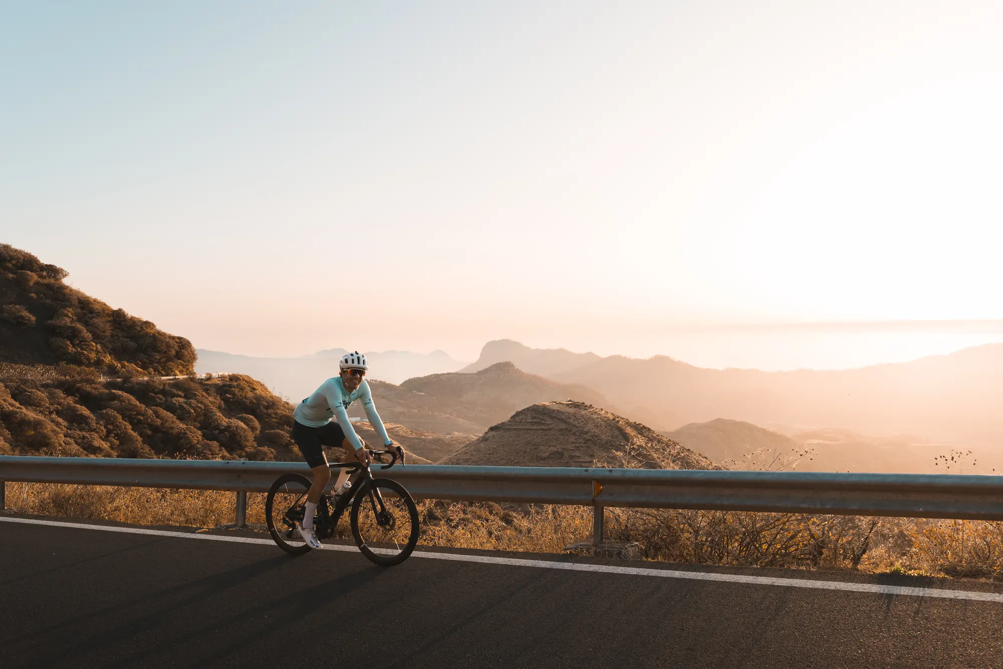 A rider on a mountain road at golden hour, with the ocean behind